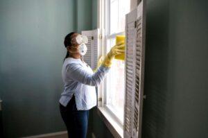 property management - Woman wearing protective gear cleans window to remove insects